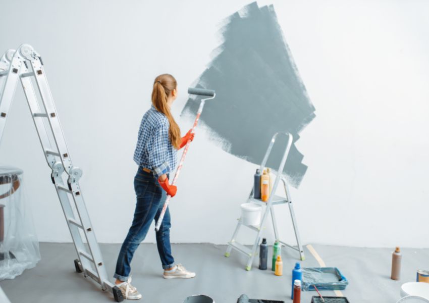 person covering a white wall with blue paint using a roller